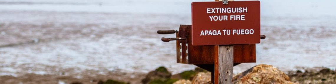 A warning sign on a beach advises to extinguish your fire in English and Spanish.