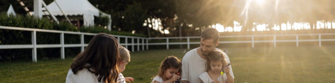 Family sitting on grass enjoying leisure time outdoors, with sun setting in the background.